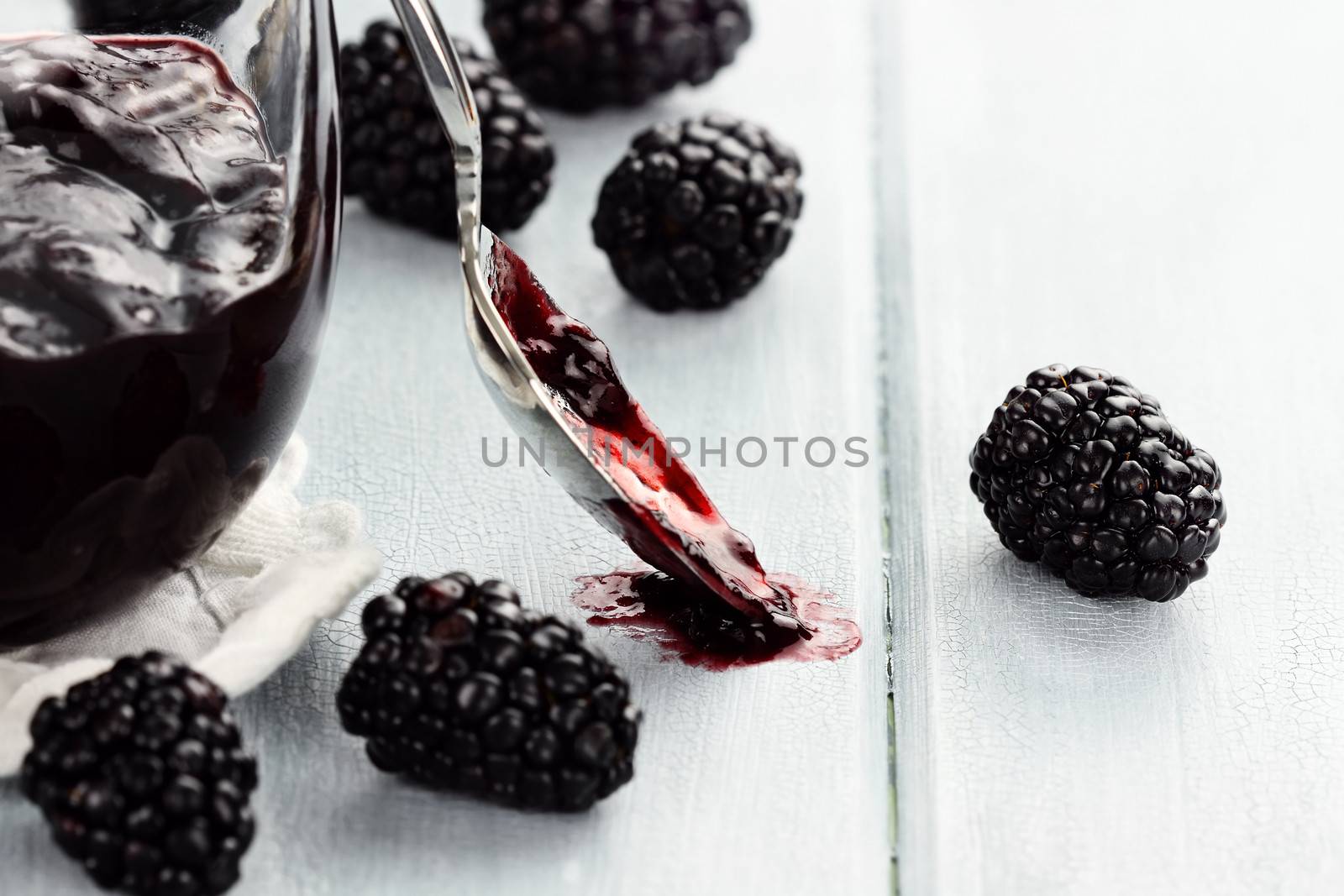 Messy spoon with blackberry jelly on a blue table. Extreme shallow depth of field and selective focus on jelly on spoon.