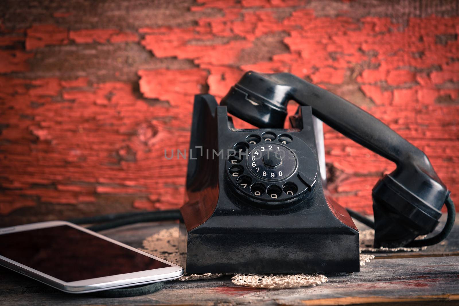 Old rotary telephone with its receiver off the hook alongside a tablet computer showing the old-fashioned and modern forms of communication against a grungy wooden wall with peeling paint