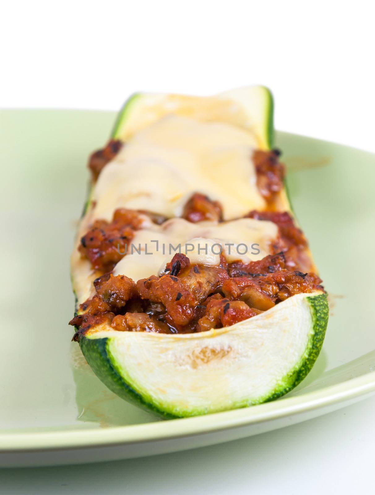 Closeup of zucchini stuffed with minced meat and cheese on green plate