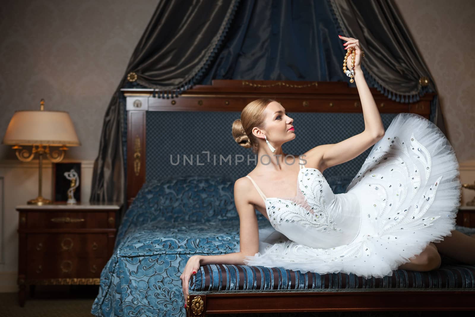Ballerina on bed at home looking at pearl necklace by photobac