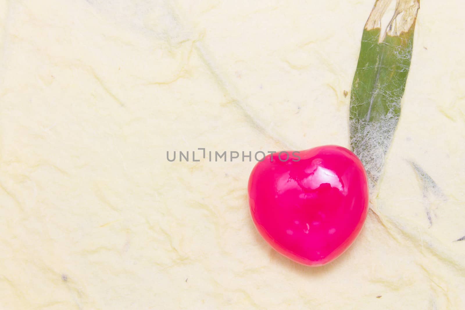 One heart candy in red color on light yellow mulberry paper background.