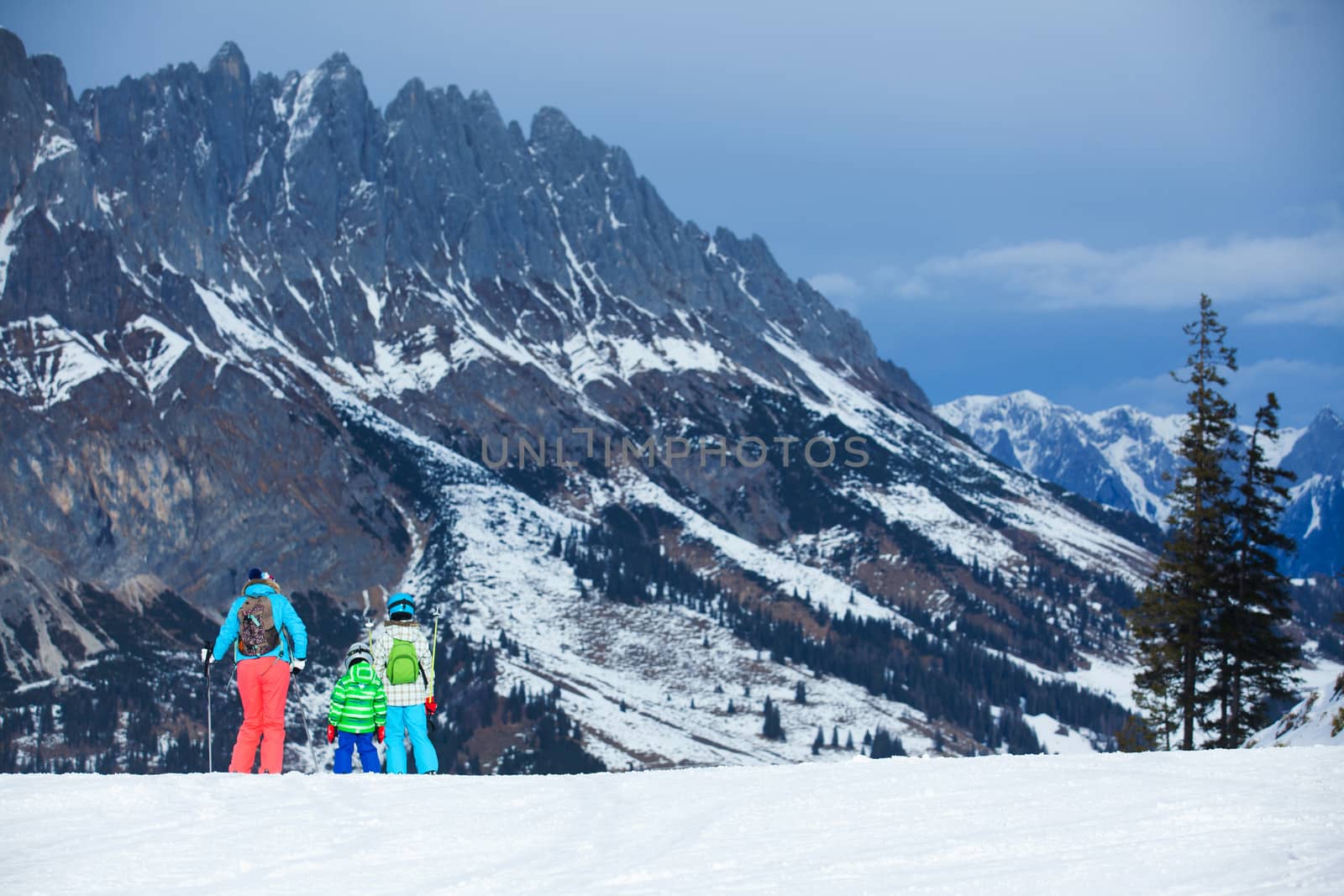 Ski, winter, snow, skiers, sun and fun - family enjoying winter vacations. Mother with her kids watching mountains. Back view
