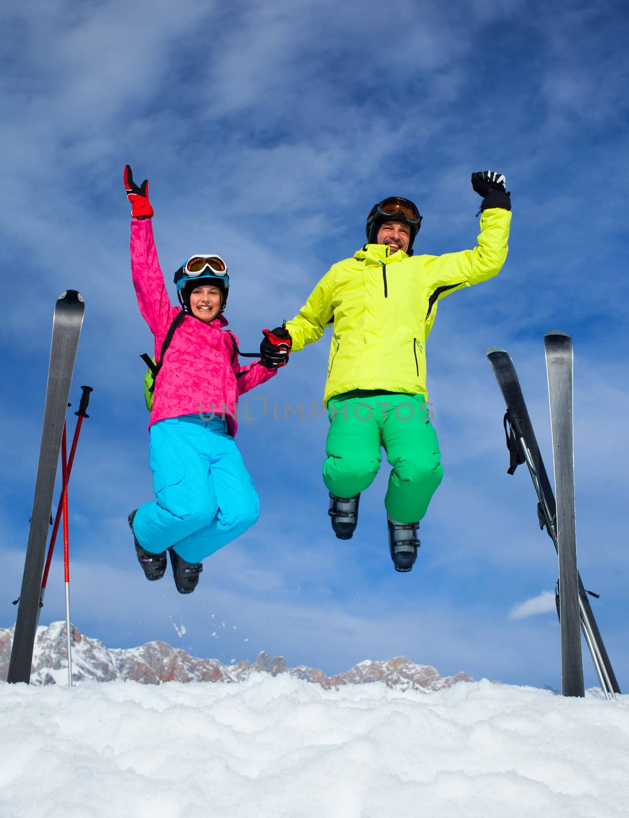 Ski, winter, snow, skiers, sun and fun - family enjoying winter vacations. Father with his daughter jumping against blue sky.