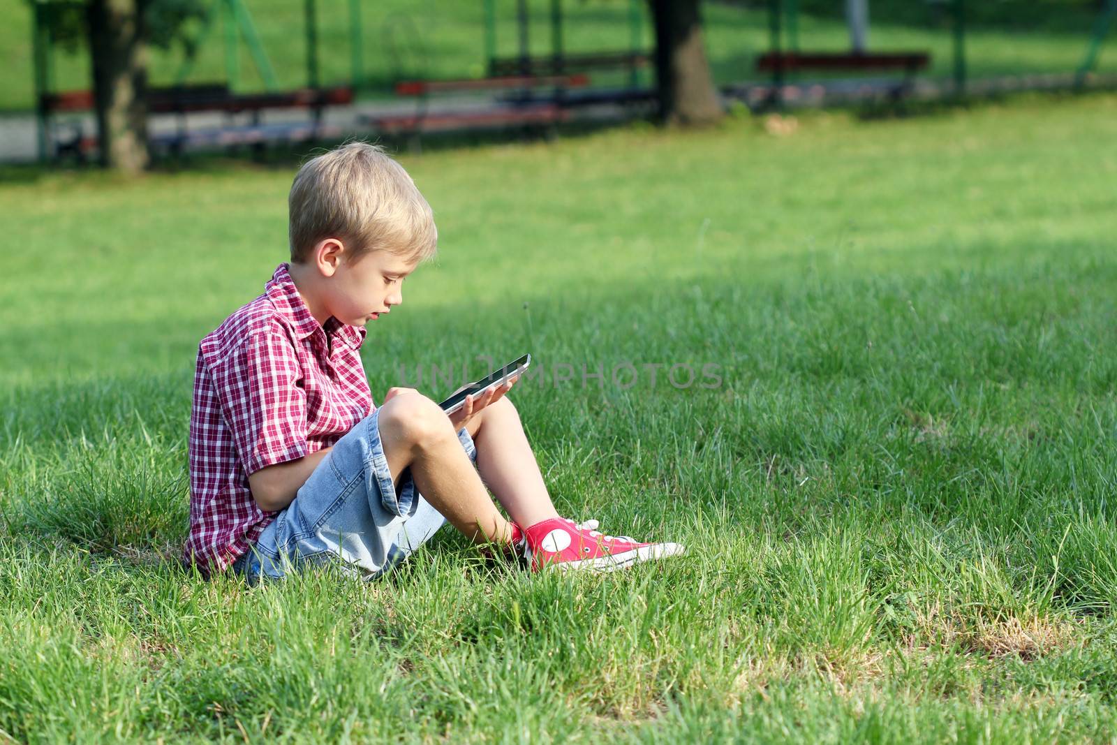 boy sitting on grass and play with tablet pc by goce