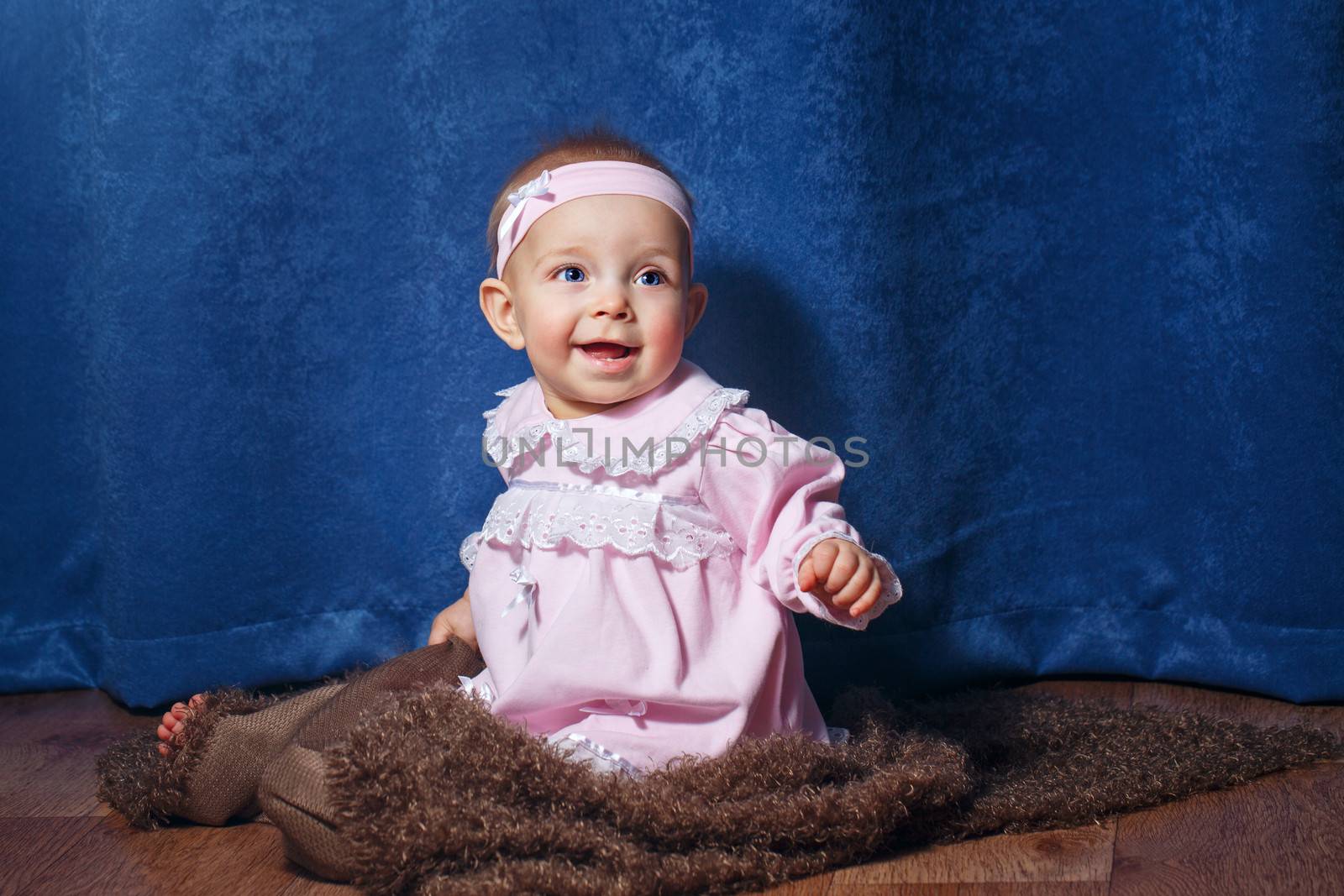 Pretty blue-eyed girl in a pink dress sitting on the floor