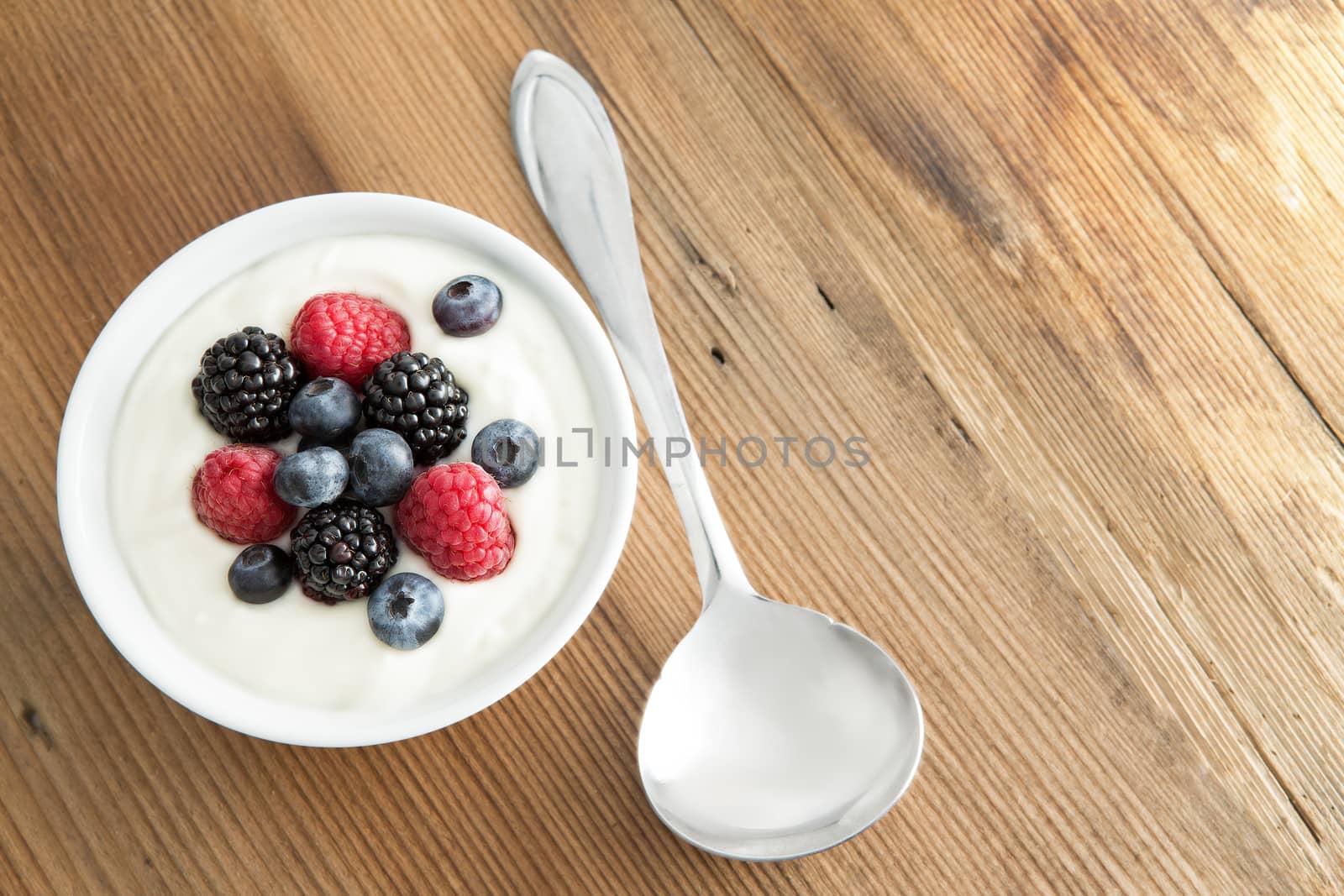 Assorted fresh berries with creamy yogurt including strawberries, blackberries and blueberries, served on a wooden table with copyspace, high angle view