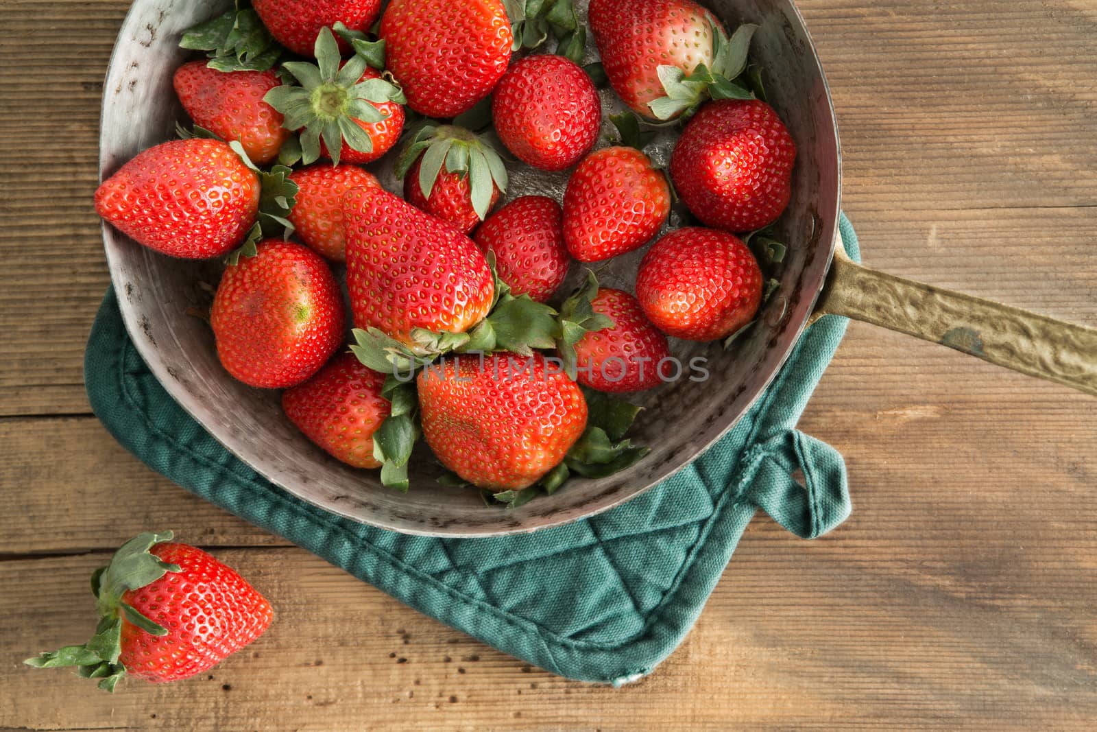 Bowl of freshly harvested ripe red strawberries waiting on a wooden kitchen counter to be made into jam, over head view