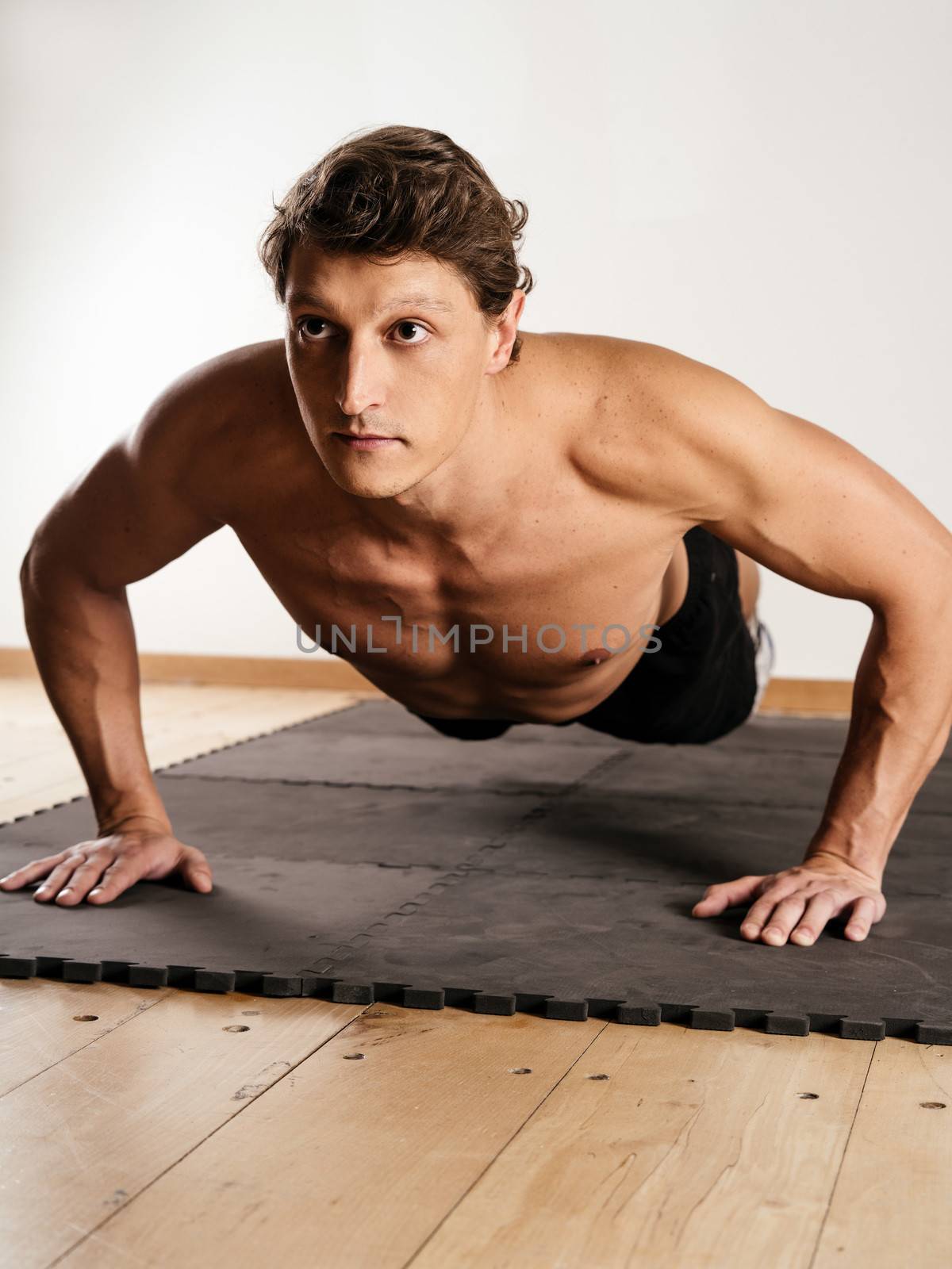 Photo of a man in his early thirties doing pushups on a mat in a fitness centre.
