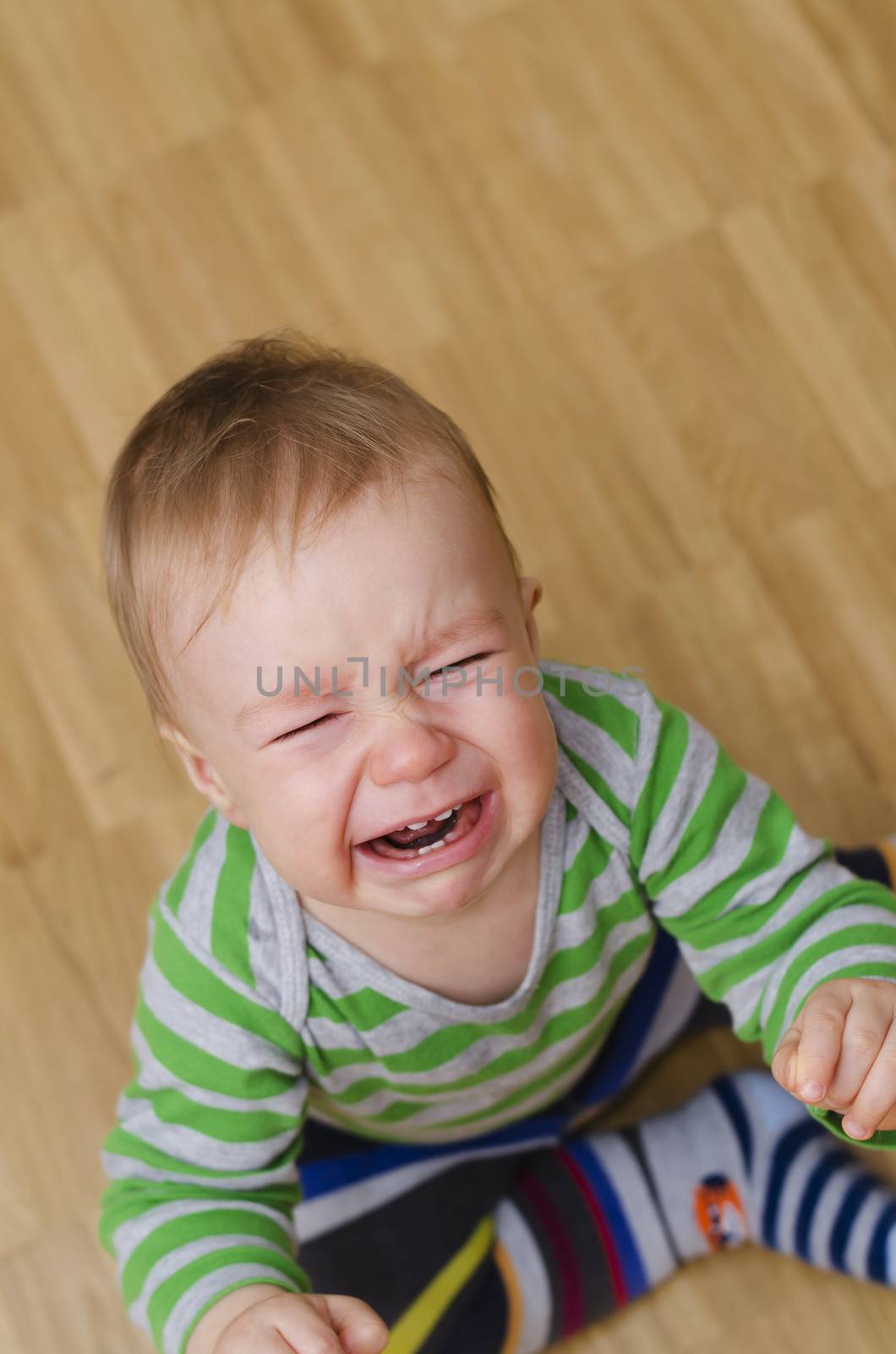 portrait of a crying baby boy sitting on the floor