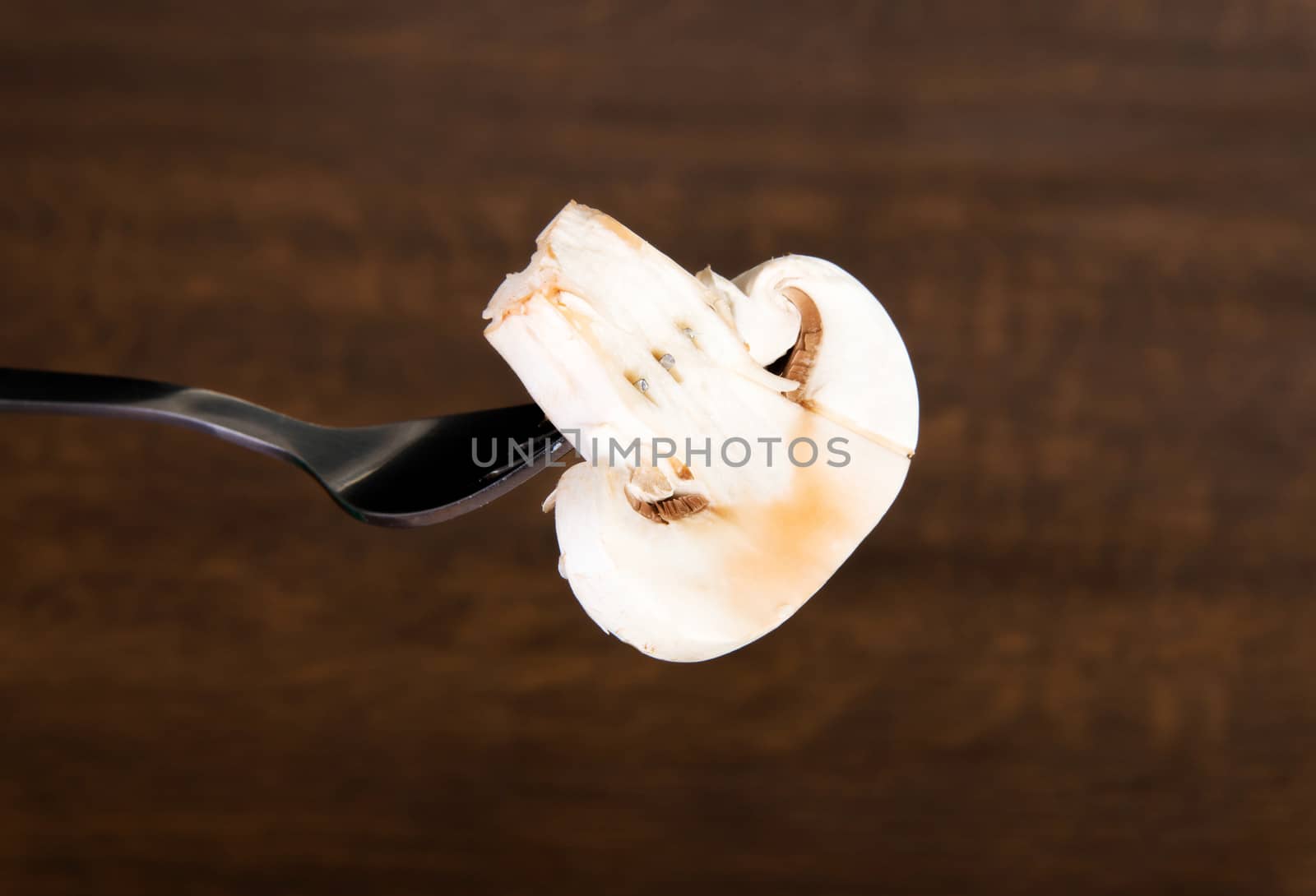 One sliced mashroom on a fork. Over wooden background.