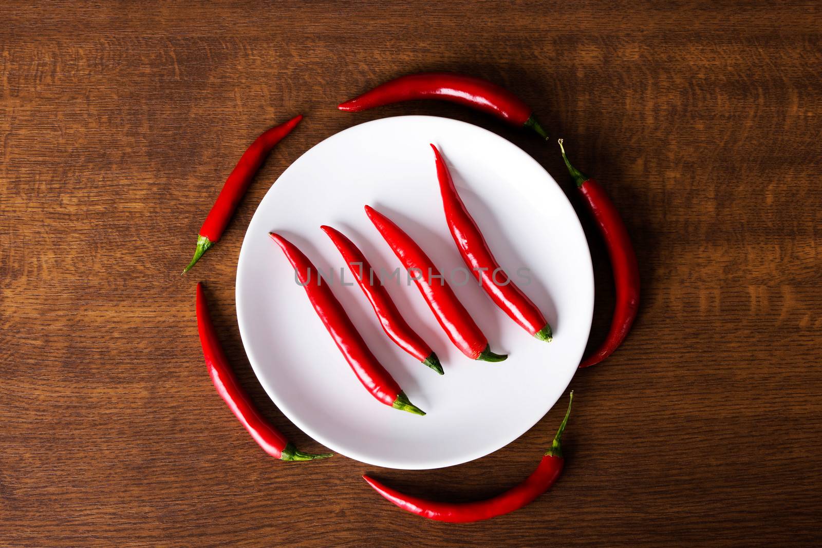 Composition of red chili peppers around white plate.