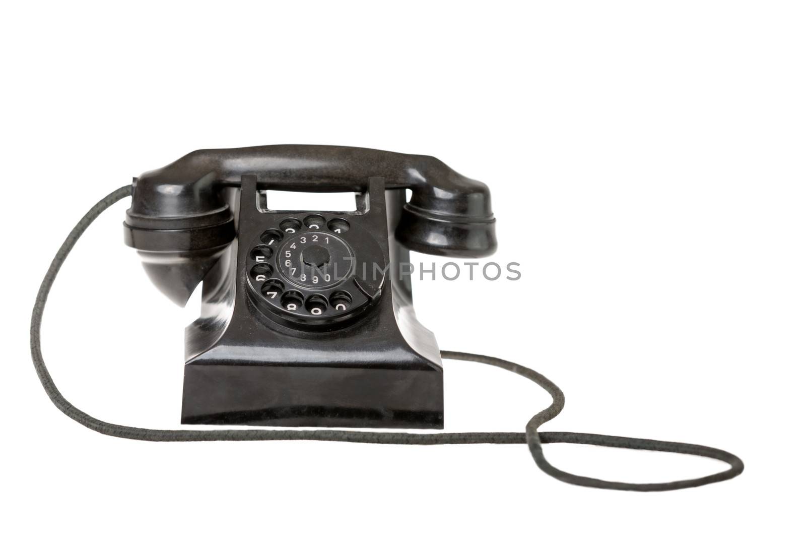 Old-fashioned black rotary telephone instrument with its handset on the cradle on a white background with a reflection and copyspace