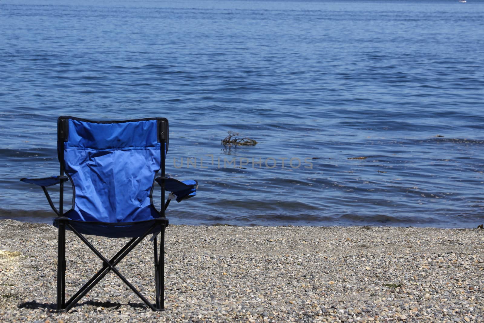 A blue chair on the beach inviting someone to relax.