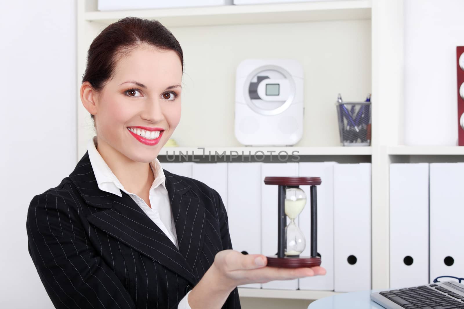 Business woman holding hourglass. Sitting in an office.