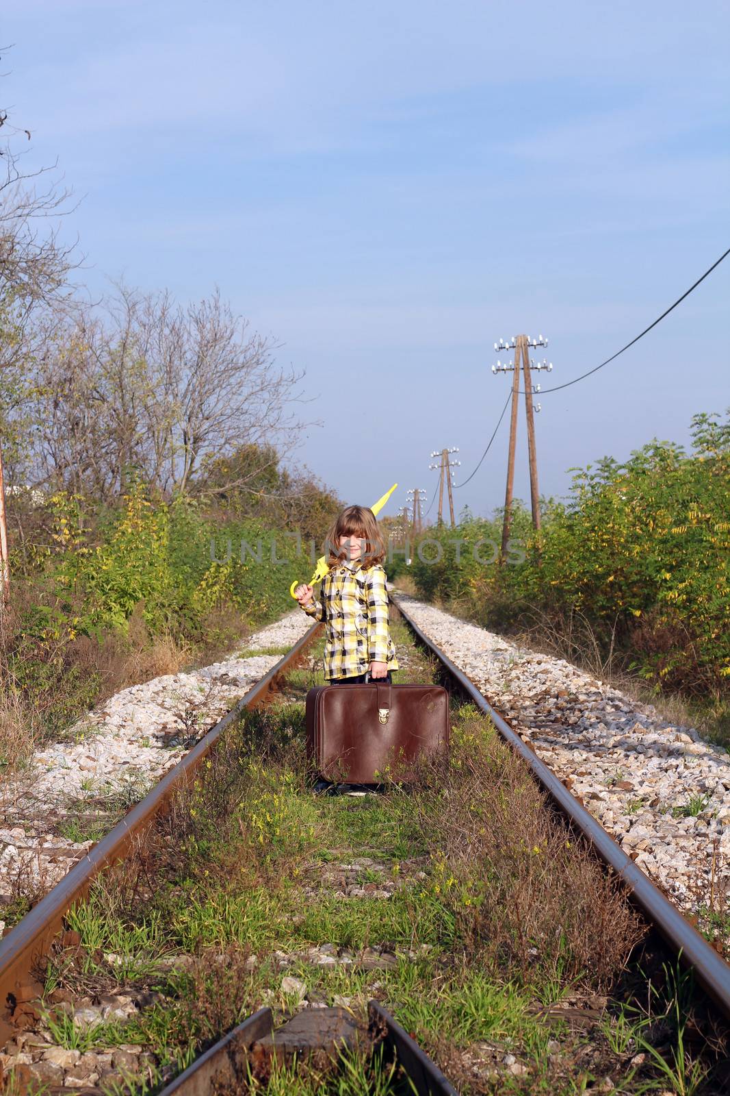 little girl with suitcase and umbrella standing on railroad