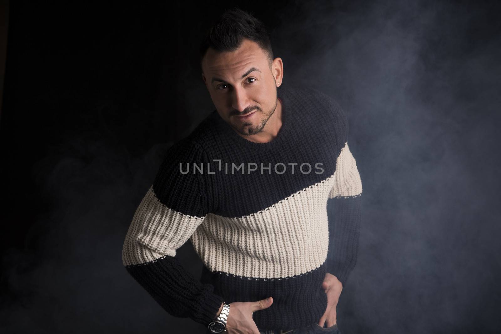 Good looking man standing, wearing winter sweater on dark background with smoke