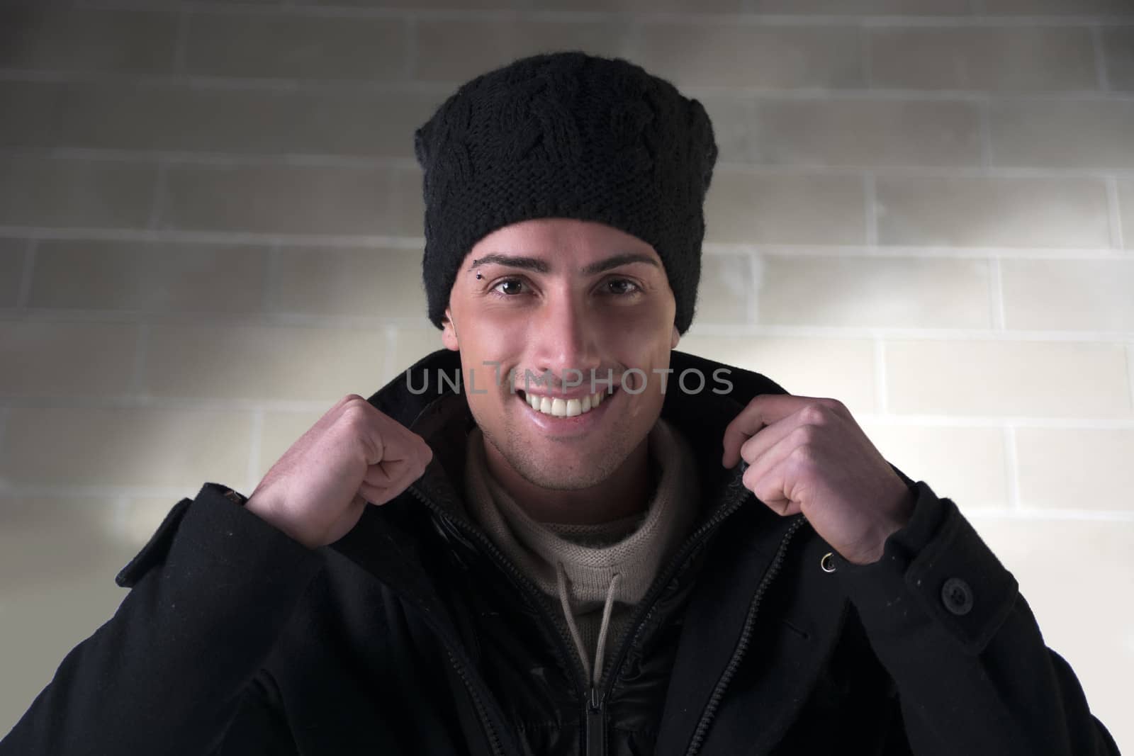 Smiling young man with wool hat and winter coat, indoors, looking at camera