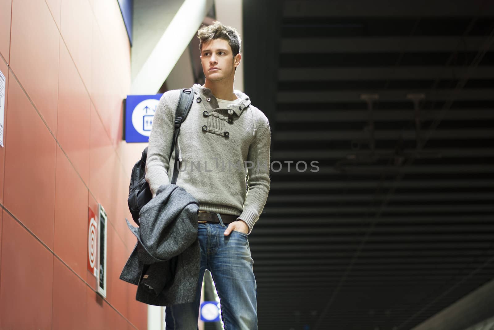 Handsome young man standing in train or subway station looking to a side, shot from below