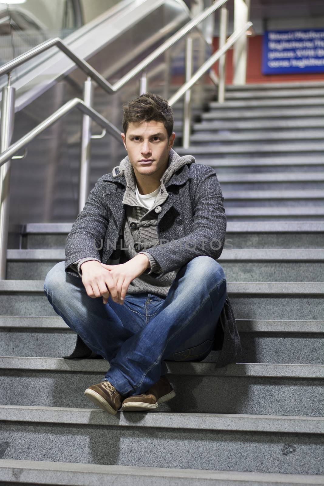Handsome young man sitting on stairs' marble steps, looking at camera