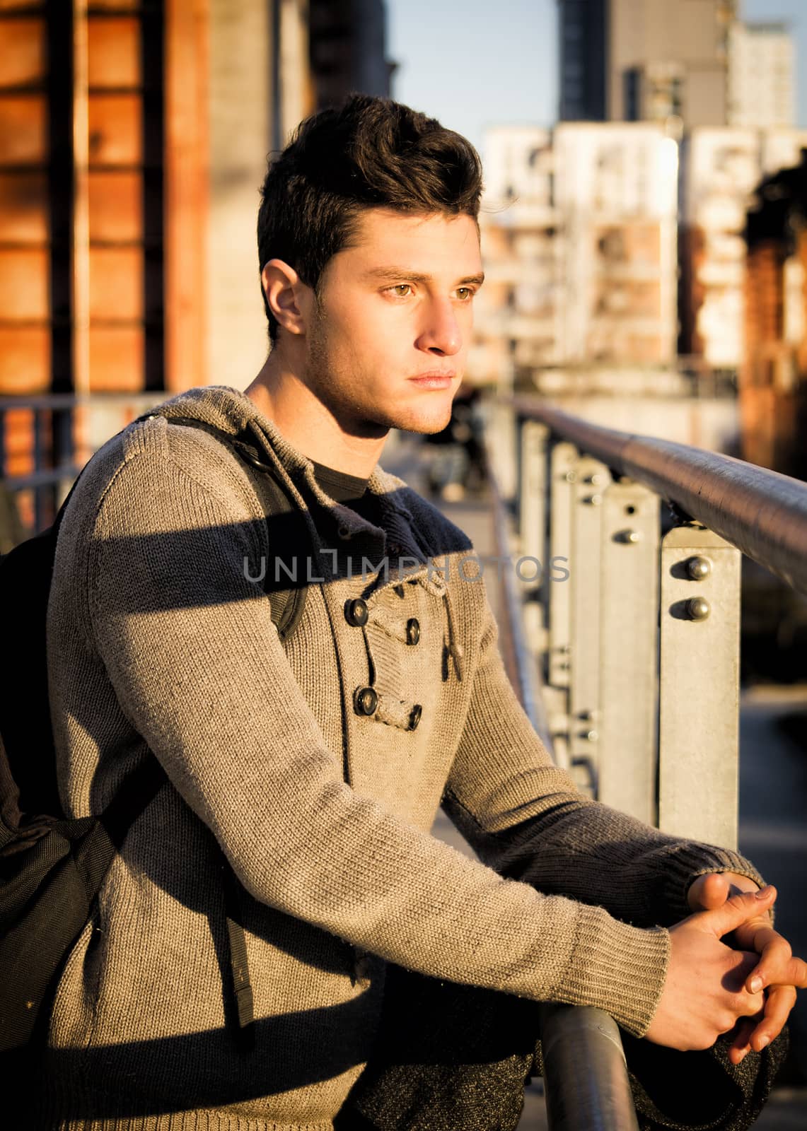 Handsome young man in city setting, lit by sunset light, looking away