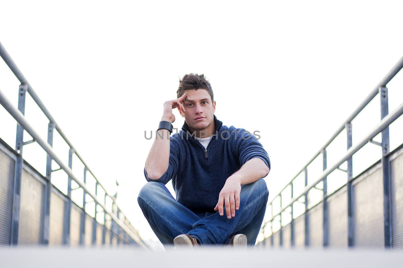 Handsome young man sitting between handrails in walkway, looking at camera
