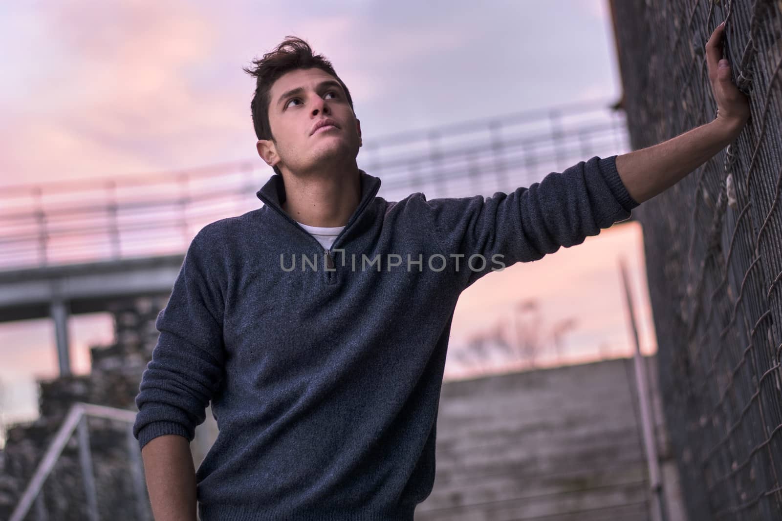 Attractive young man in urban setting, evening time, leaning against wall
