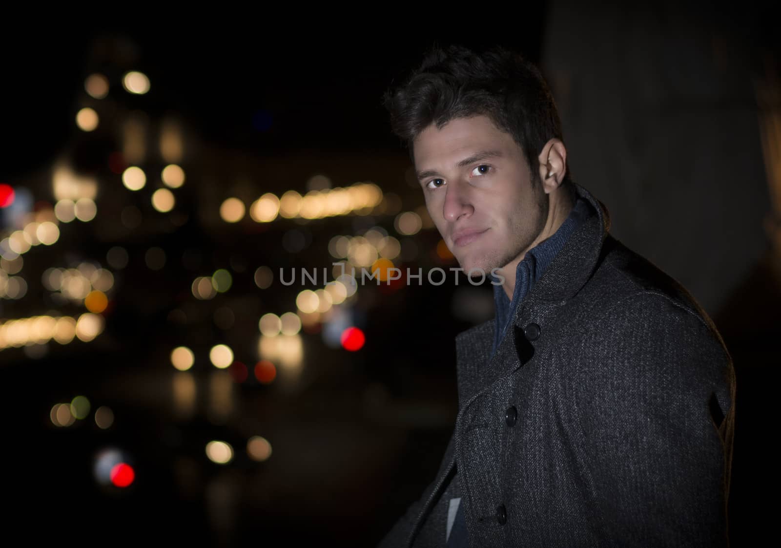 Attractive young man portrait at night with city lights behind him, looking at camera