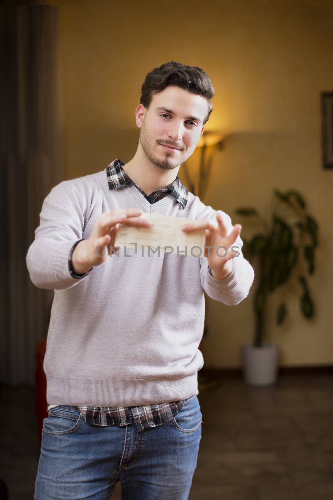 Handsome young man holding check in his hands, smiling and looking at camera