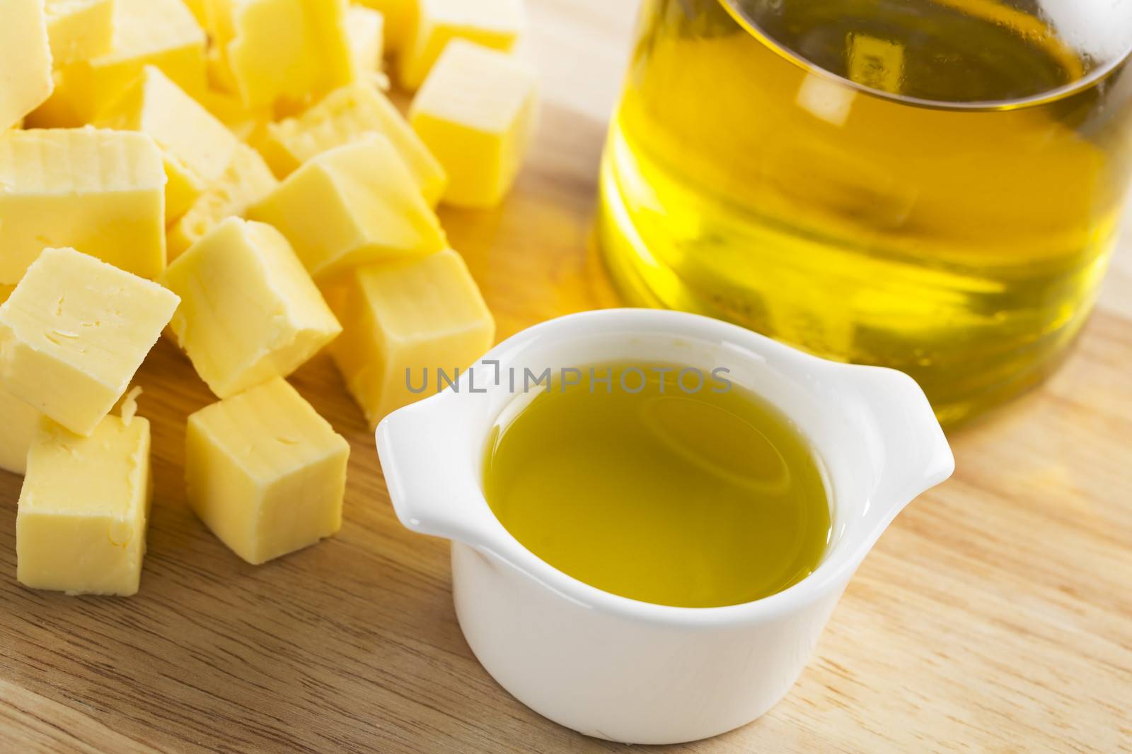 Olive oil in small glass container with bottle of oil and cubes of butter