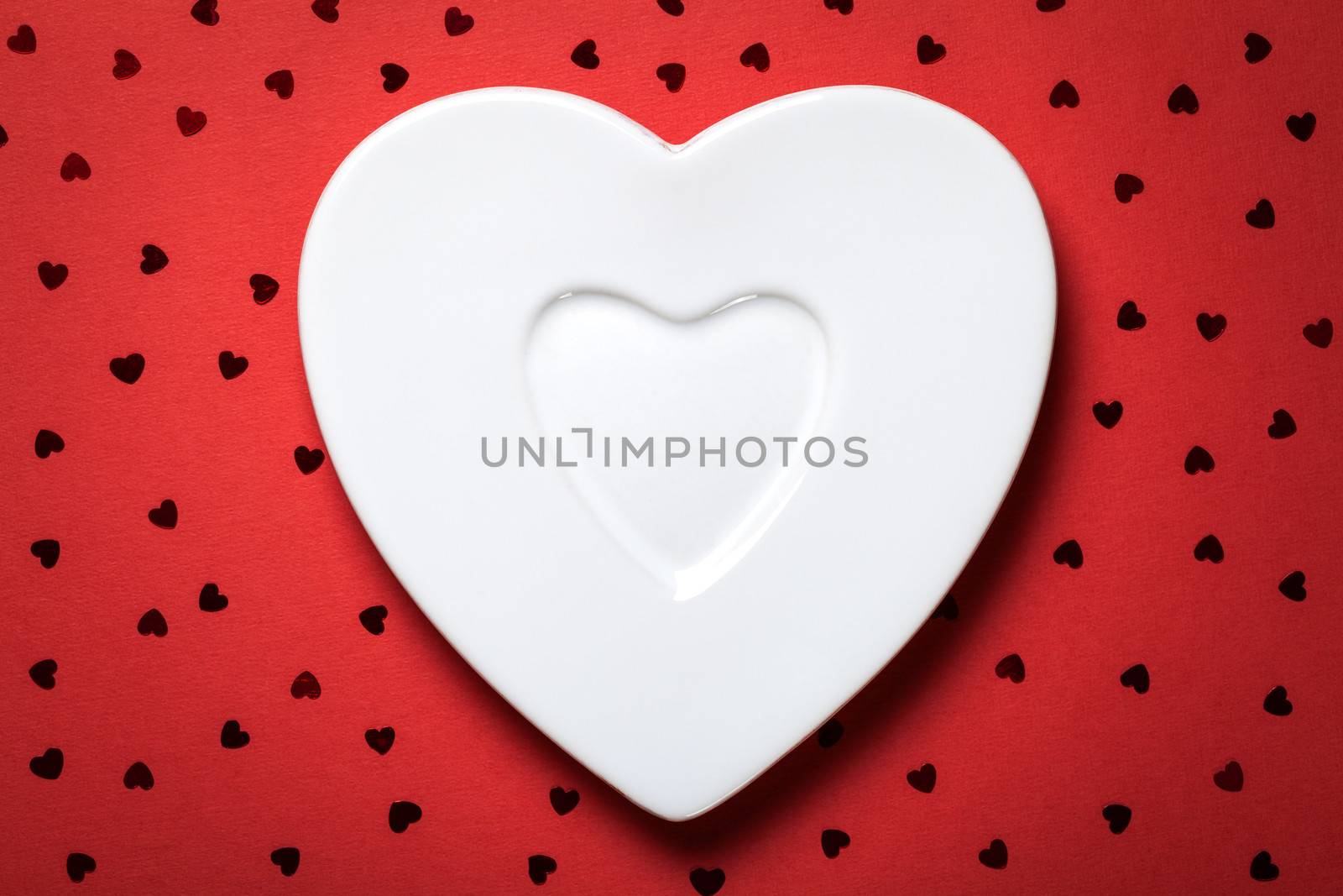 Heart form white plate on red paper background. Top view 