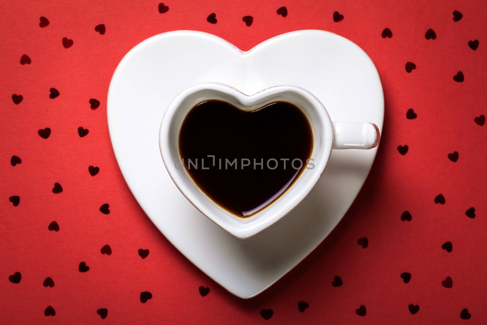 Coffee cup in shape of heart on red paper background. Top view