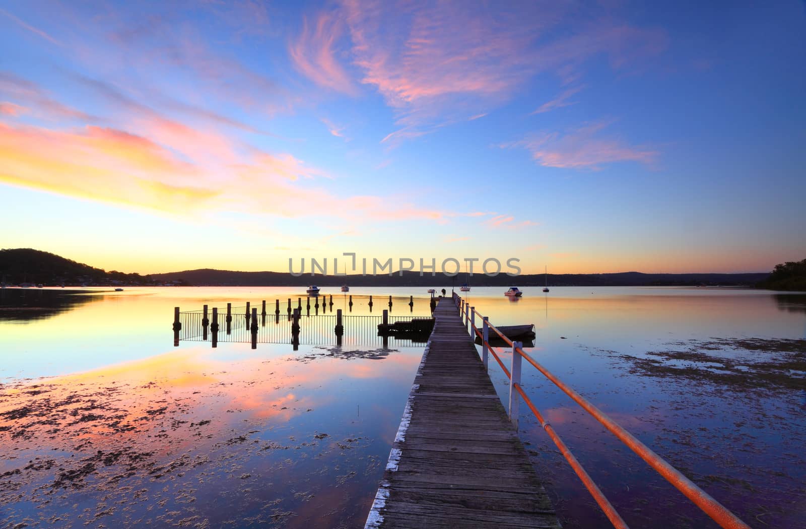 Vivid and colourful sunset at mid tide, Yattalunga Australia.   Jetty wharf and harbour pool, boats and yachts moored on the evening waters at Yattalunga, on the NSW Central Coast, Australia.  