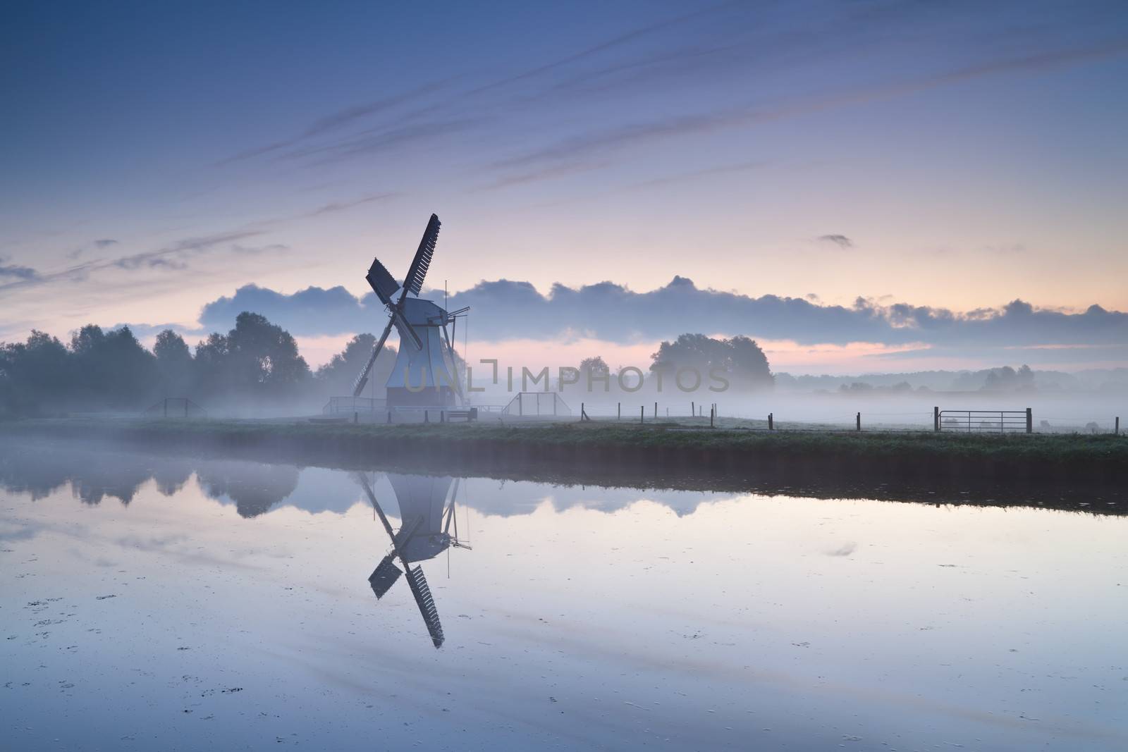 white Dutch windmill by river in misty sunrise, Groningen, Holland