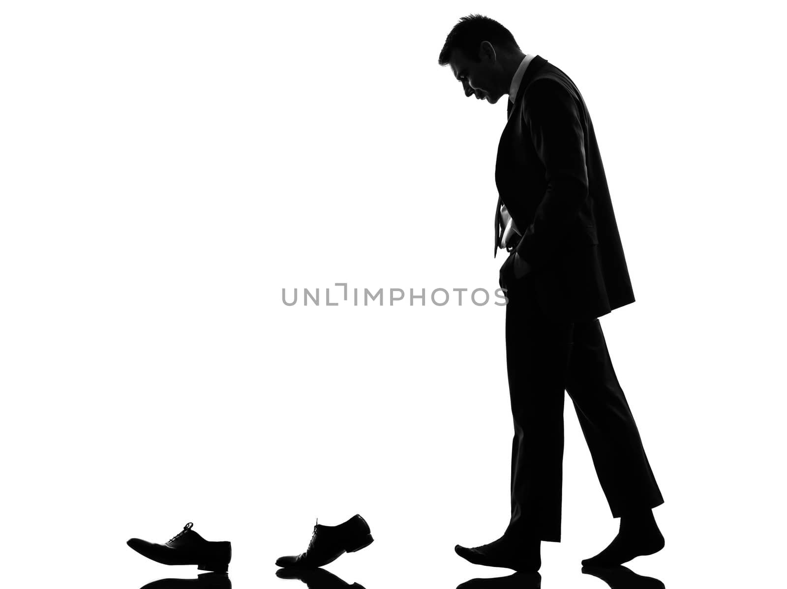 one caucasian business man walking behind his shoes   in silhouette  on white background