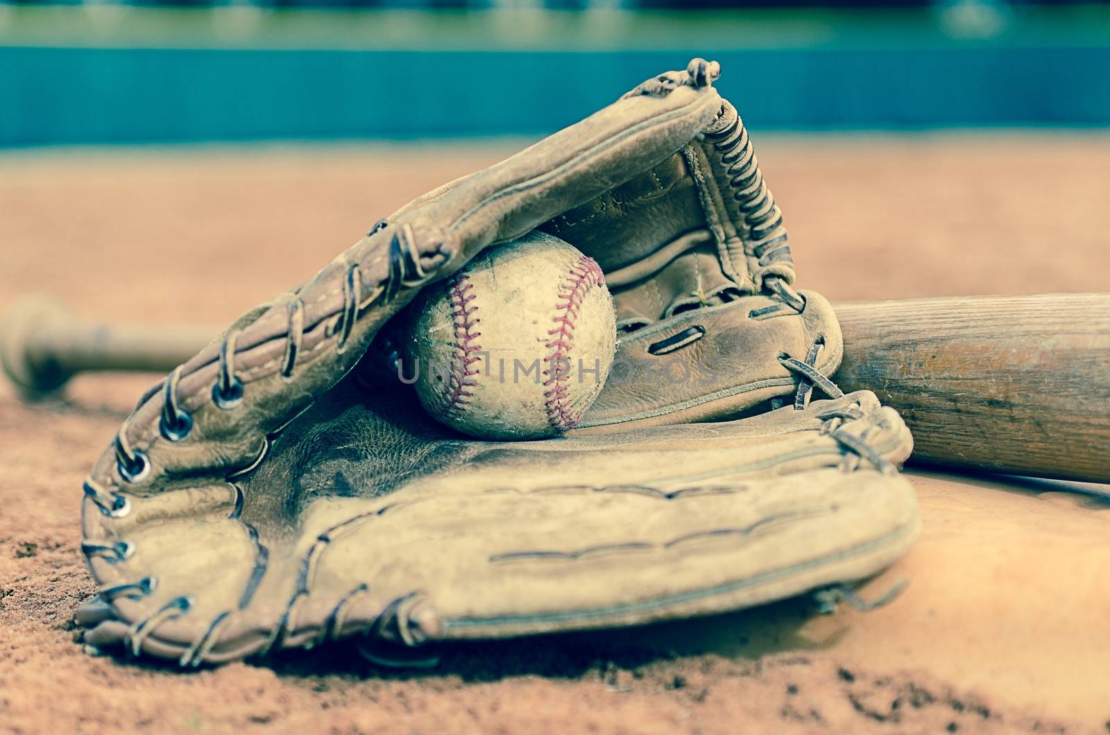 Traditional baseball with ball in glove and bat on base on field.  Outfield wall in background.