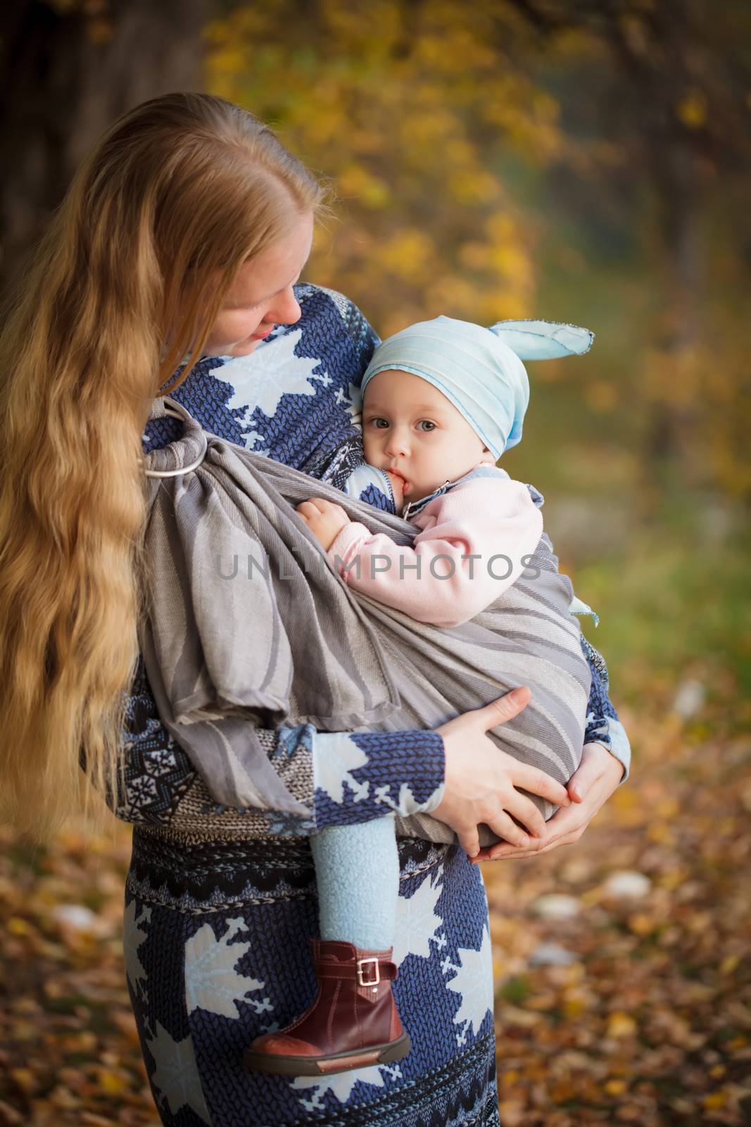 Mother walking with child outdoor, baby nursing in sling