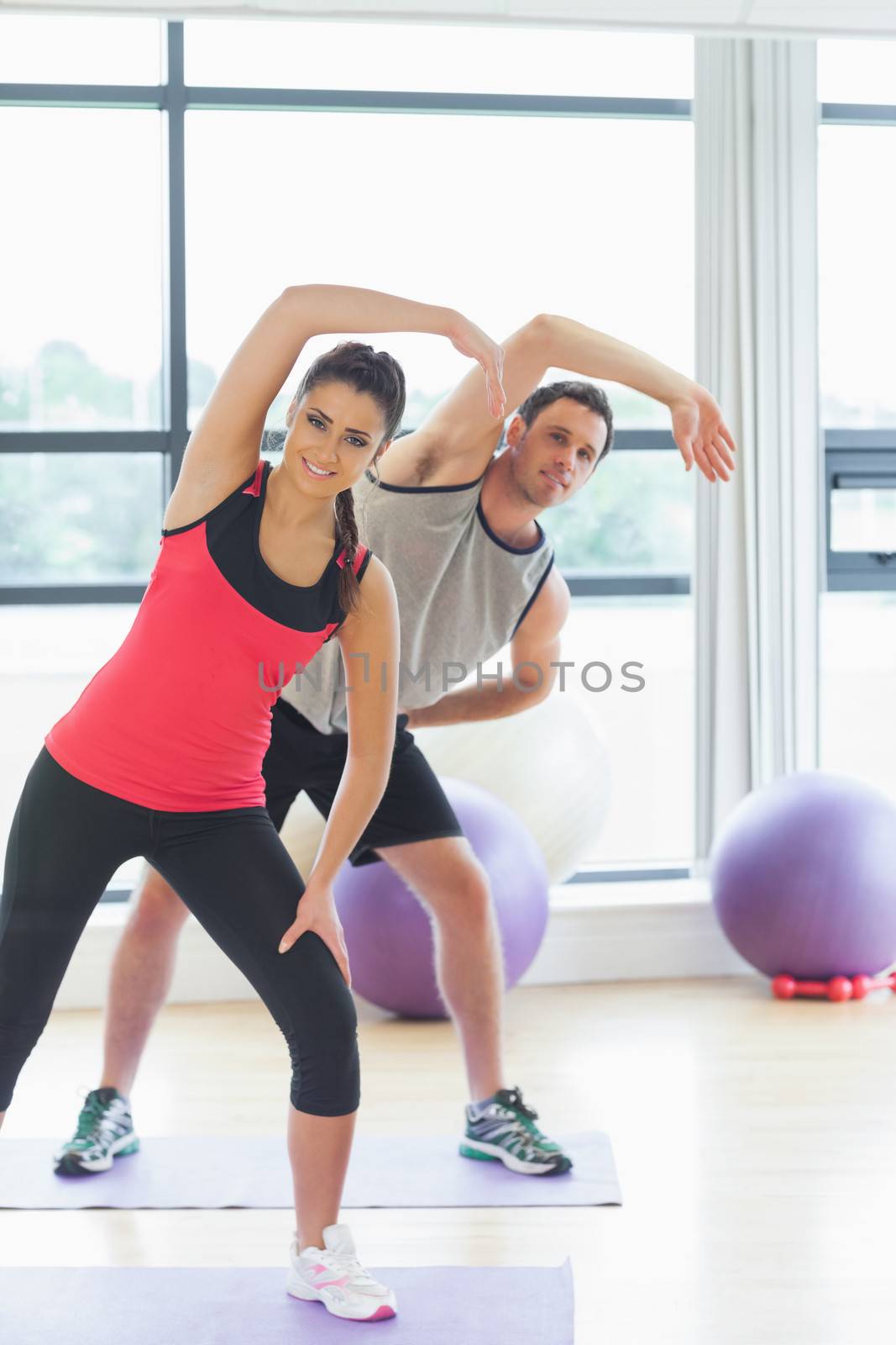 Portrait of two sporty people stretching hands at yoga class in fitness studio
