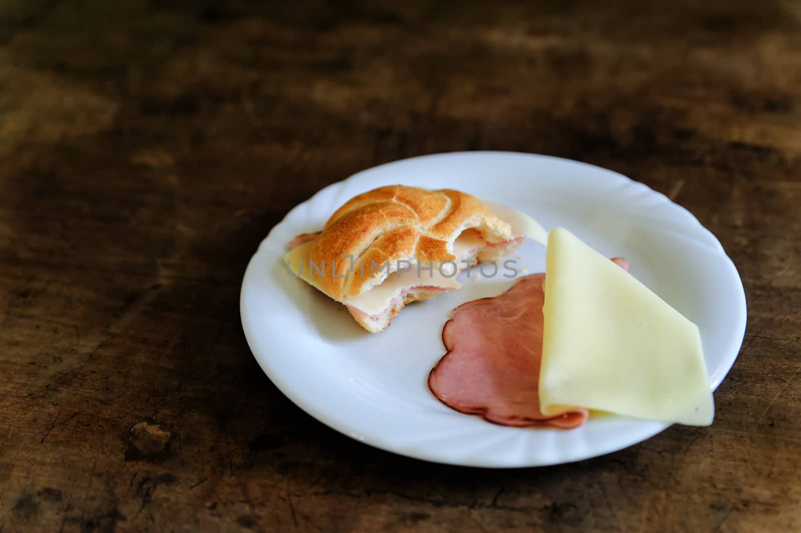 Bitten Bun with ham and cheese on a wooden table