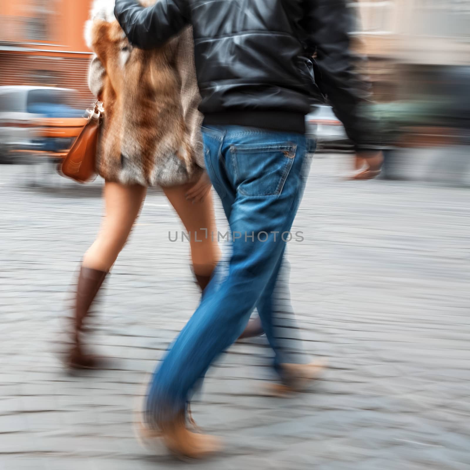 Man in jeans and a woman in a fur coat walking down the street hugging. Intentional motion blur