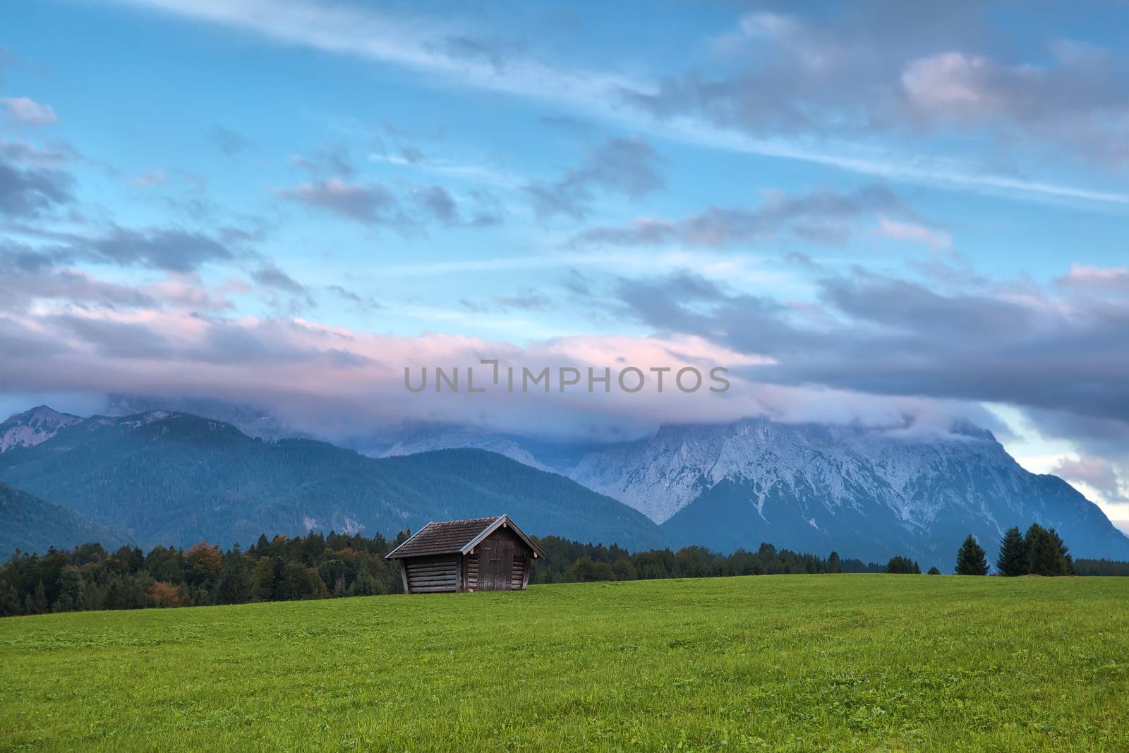 wooden hut on meadow and sunset clouds over Karwendel mountains, Bavaria, Germany