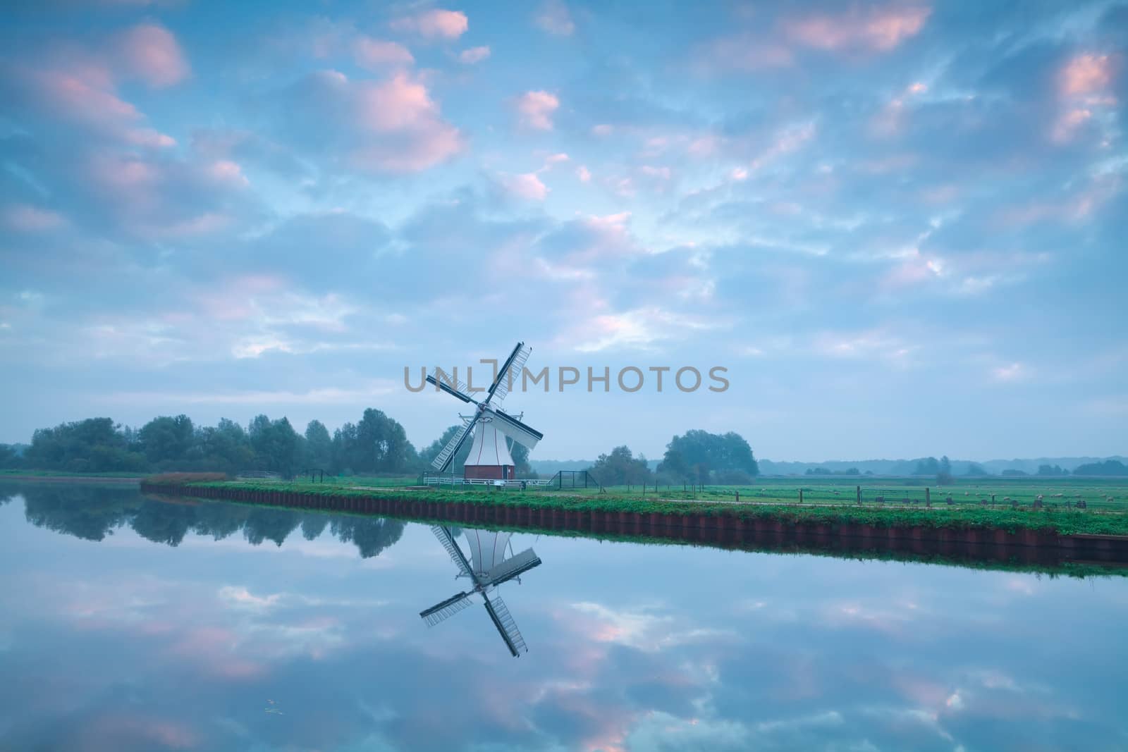 charming Dutch windmill by river during sunrise by catolla