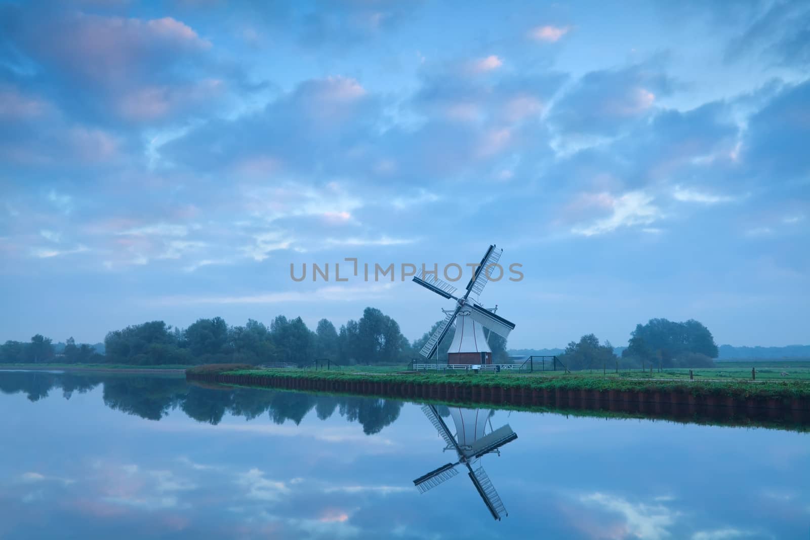 Dutch windmill close to river during calm pastel sunrise, Holland