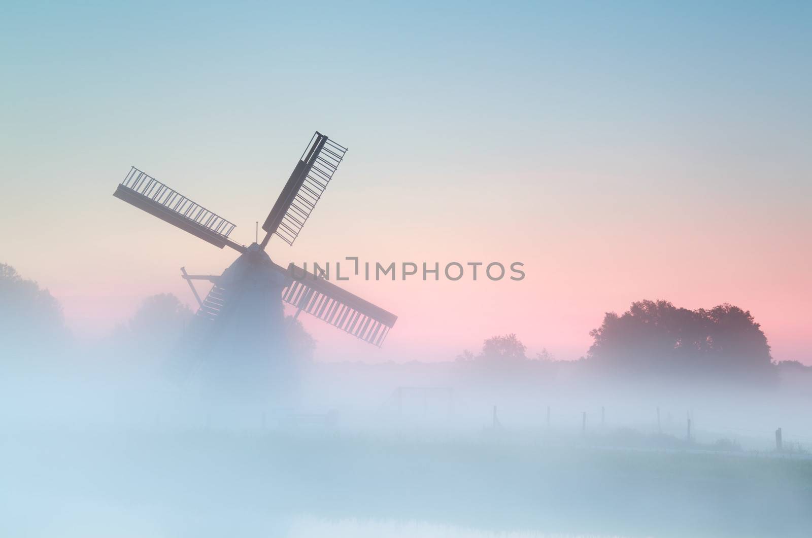 charming Dutch windmill in dense sunrise fog by catolla