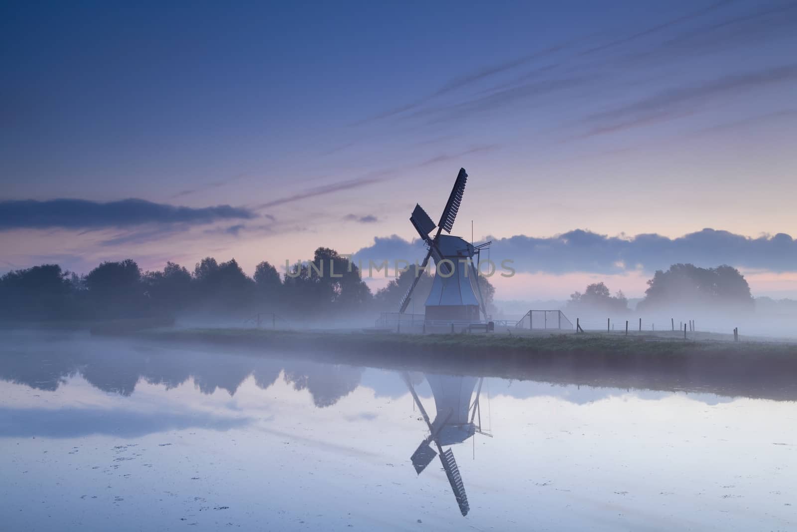 Dutch windmill reflected in river in sunrise fog by catolla