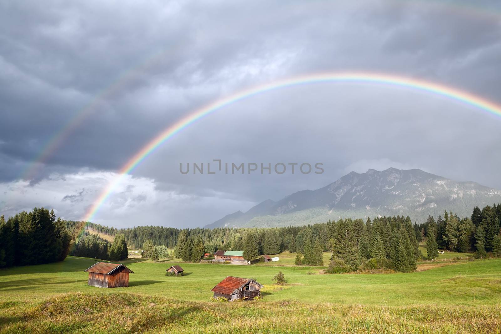 colorful rainbow over alpine meadows with wooden huts by catolla