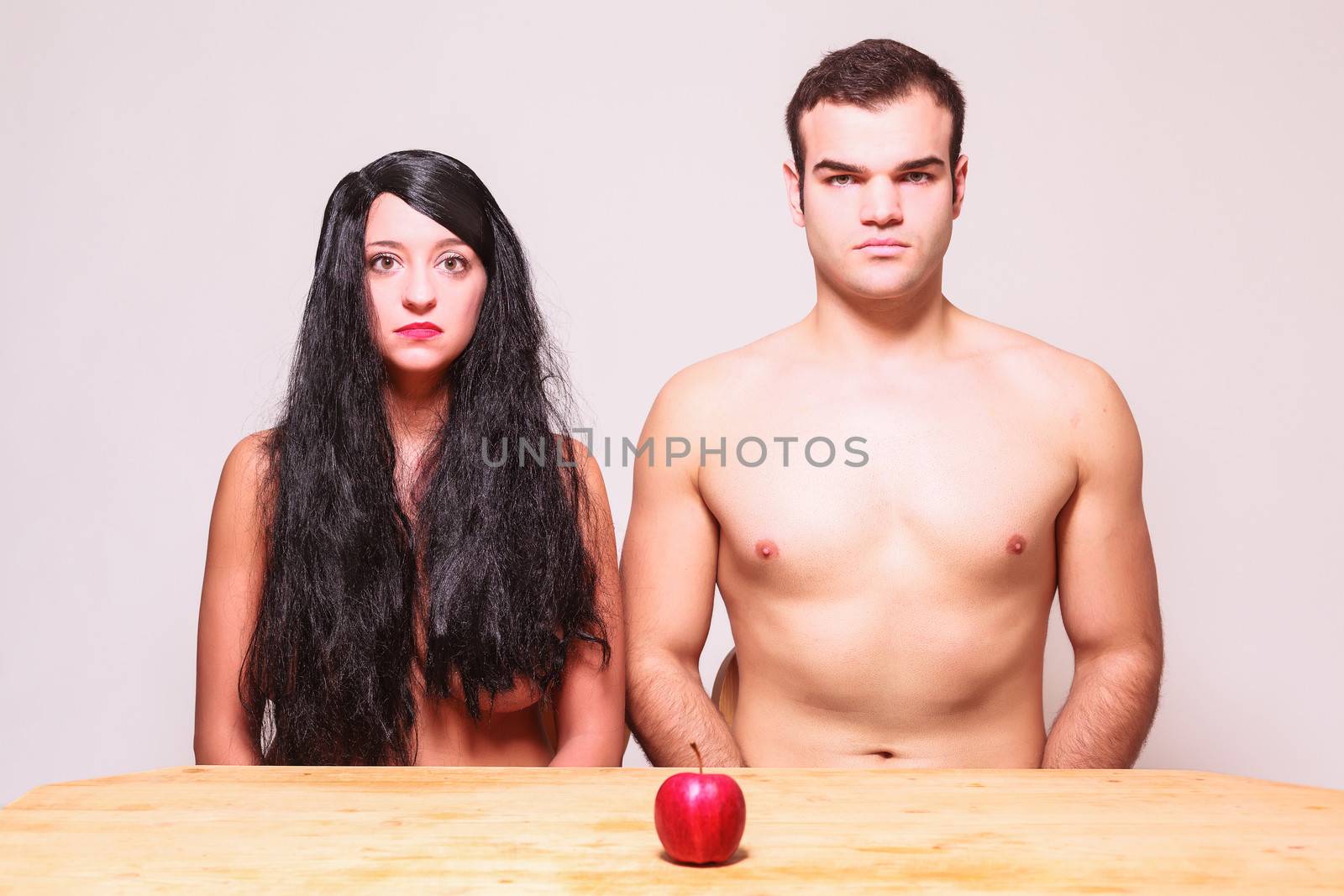 The apple of temptation sitting on a wooden table in front of a naked couple conceptual of a modern day Adam and Eve
