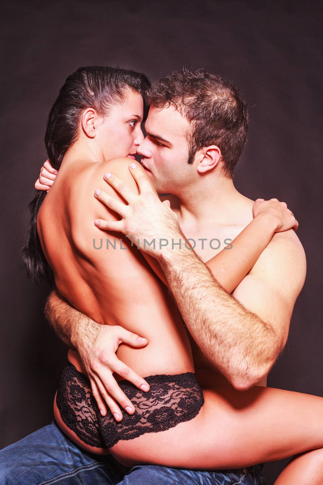 Romantic couple in a suggestive erotic pose with the woman sitting on the mans lap in her panties indulging in passionate foreplay,