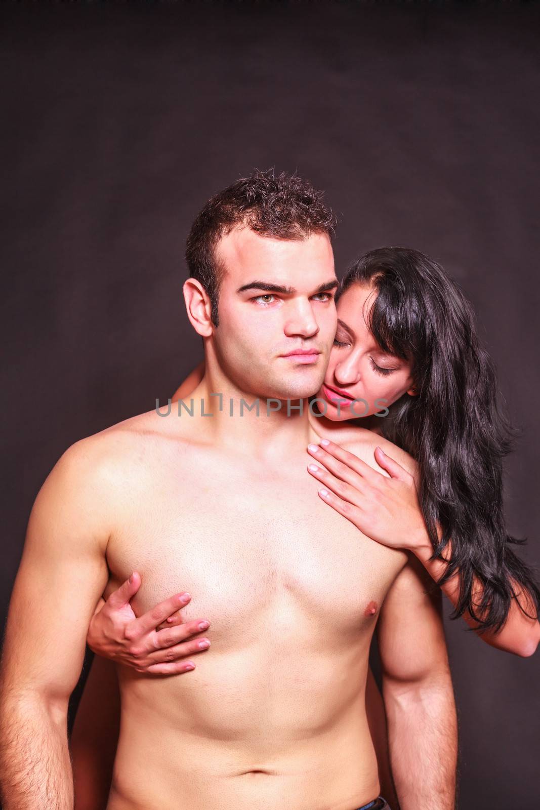 Seductive passionate woman running her hands over the naked body of a handsome young man as she nibbles at his neck from behind