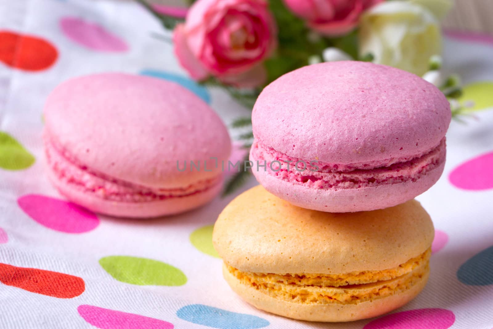 Multicolored macaroon on colorful tablecloth near flowers