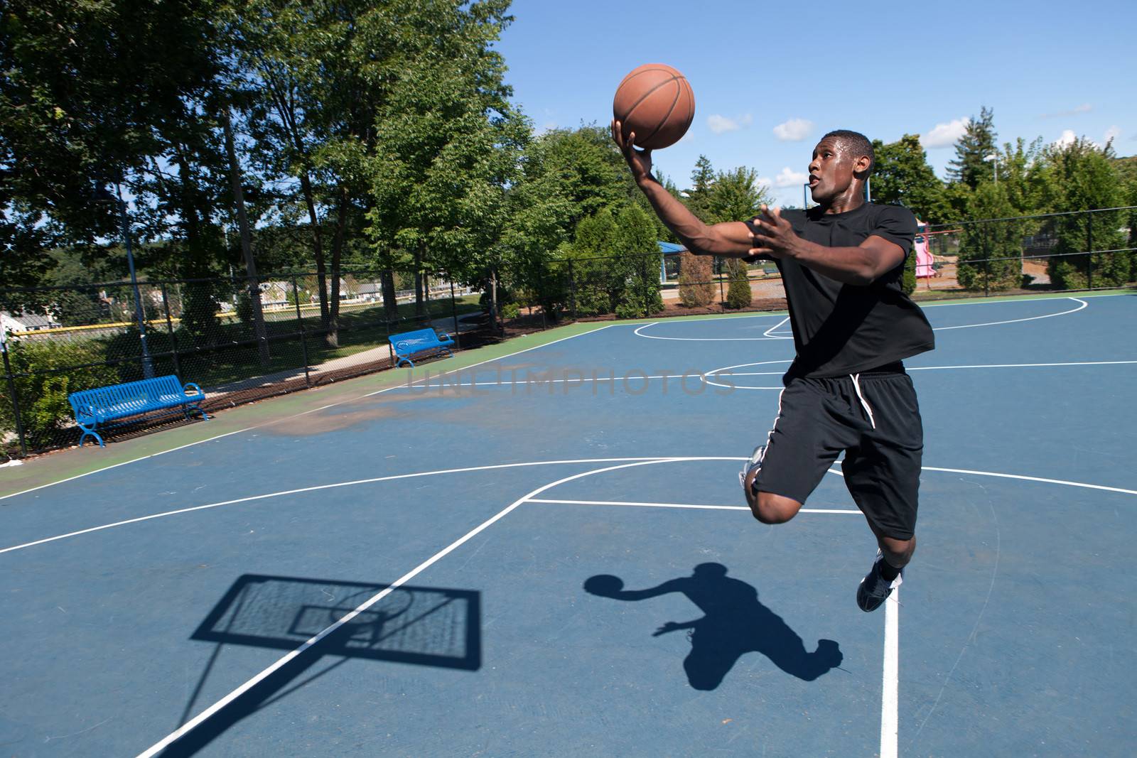 Basketball player driving to the hoop for a layup. Shallow depth of field. Contrasty shadow silhouette of backboard and player clearly visible.